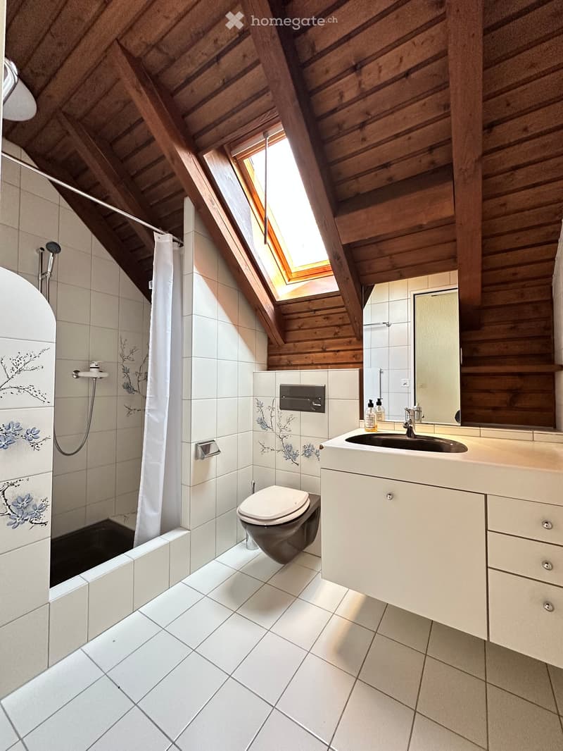 Bathroom with white tiles, wooden ceiling, shower, toilet, sink, mirror, and skylight