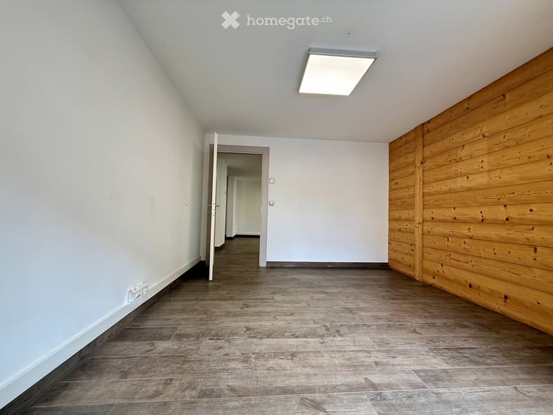 Empty room with white walls, wooden floor, open door, and a wooden wall on the right side.