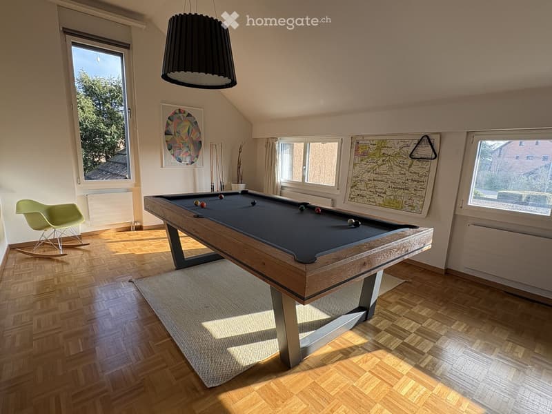 Billiard room with a wooden pool table, a green rocking chair, a white rug, a black lamp, and a map on the wall.