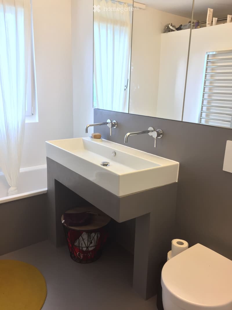 Bathroom with white sink, gray wall, white toilet, white shower curtain, yellow rug, and a basket with towels