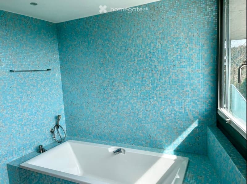 Bathroom with blue tiled walls, white bathtub, shower head, faucet, window