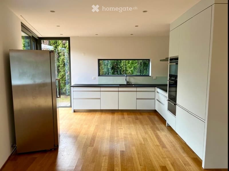 modern kitchen with wooden floor, white cabinets, black countertops, stainless steel refrigerator, large window, dishwasher