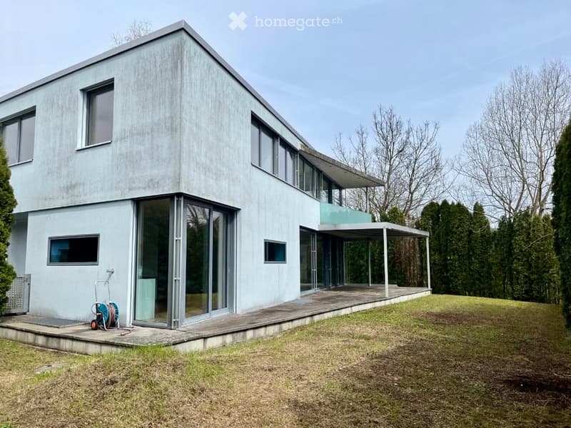 Modern house, gray exterior, large windows, wooden deck, open terrace, surrounded by grass and trees