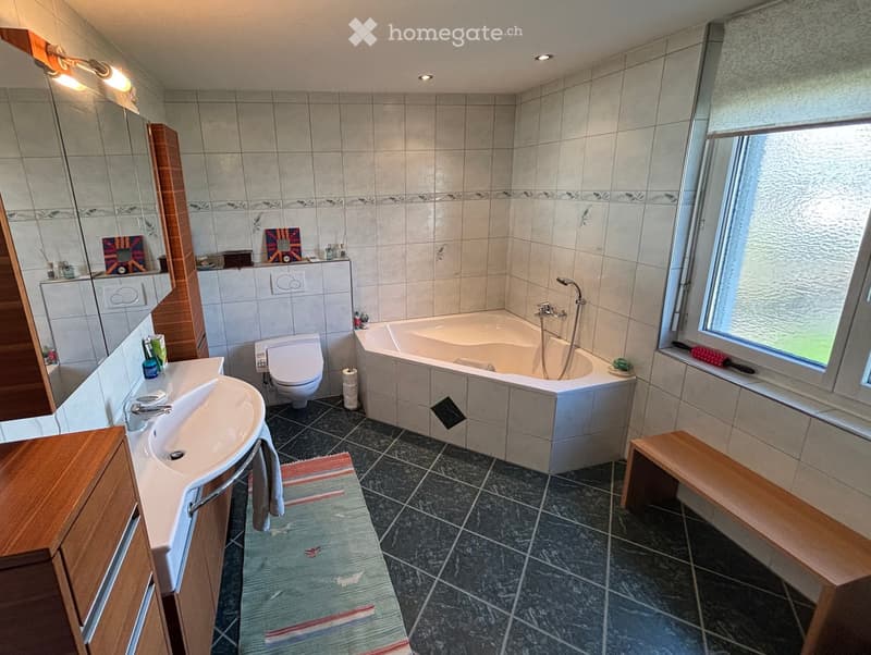 white tiled bathroom with bathtub, toilet, sink, mirror and wooden furniture