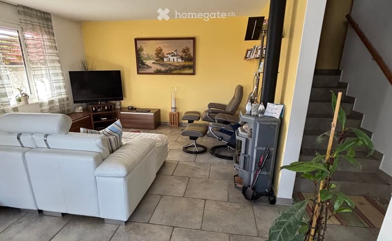 living room features a white leather couch, a white sofa bed, a wooden television stand, a flat screen television, yellow walls, three grey recliners, a wooden cabinet, a plant, an open fireplace, and a staircase leading up to the second floor.
