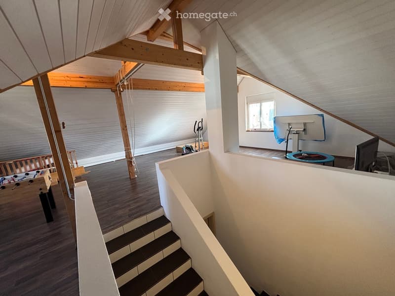 A view of an attic room featuring a staircase, an empty room with wooden beams and a window, exercise equipment, and a foosball table.