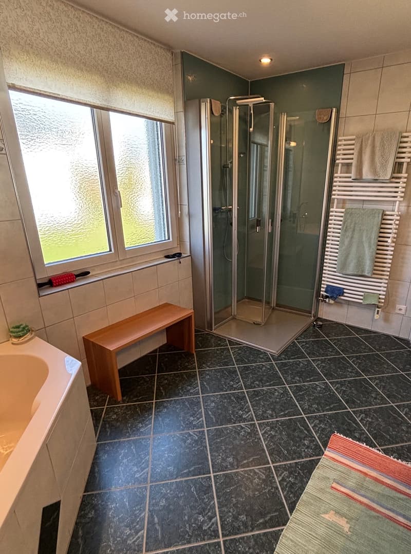 Bathroom with bathtub, glass walk-in shower, bench, radiators, towel racks, and tiled floor