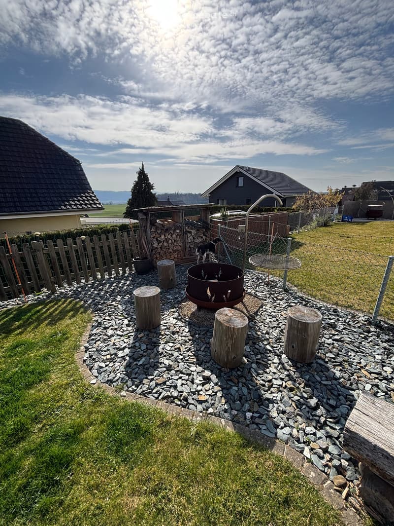 wooden fence, grass, large pile of wood, fire pit with stone benches