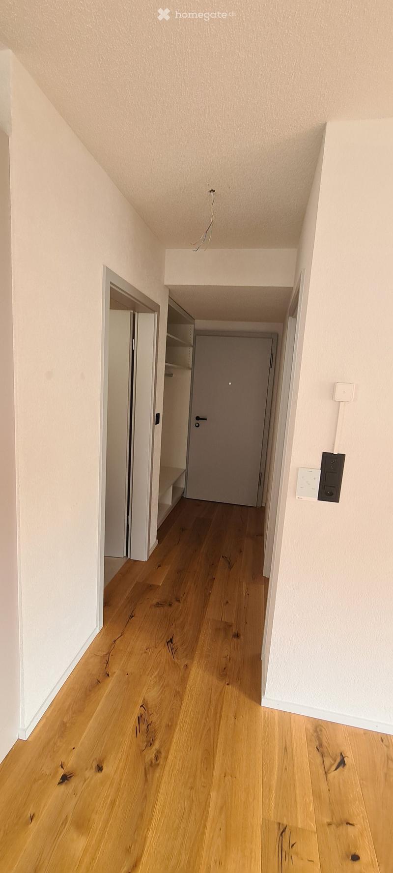 Empty hallway with wooden floor, white walls, two doors, and a white shelf