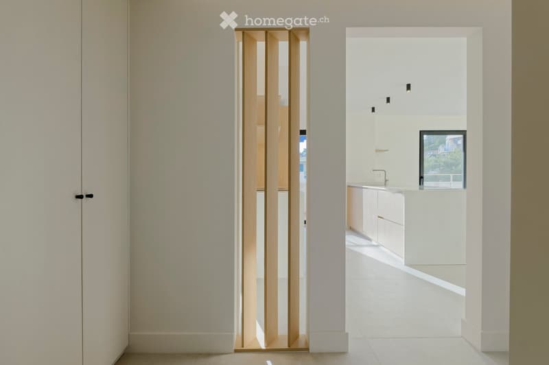 minimalist room, white walls, wooden door, white flooring, open to kitchen