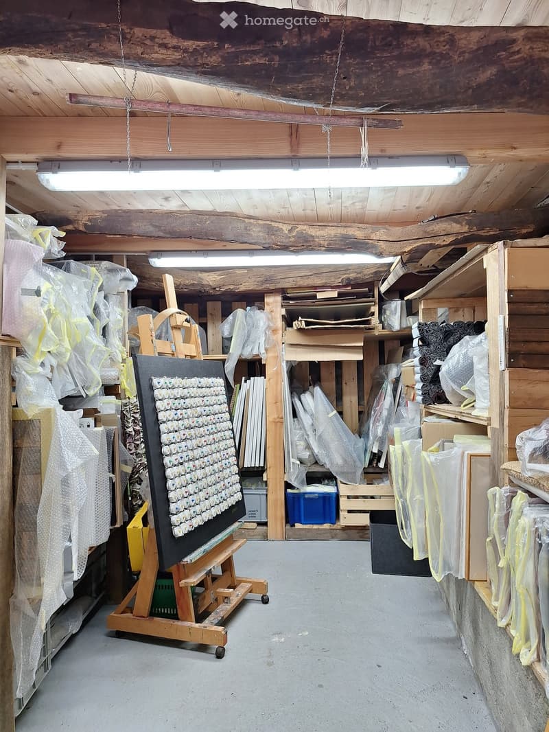 A room with wooden beams, fluorescent lights, wooden shelves, storage boxes, and a wooden easel with a canvas.