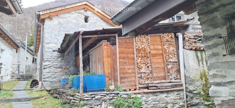 Stone house, wooden structure, storage shed, blue barrels, plants, pathway, street light