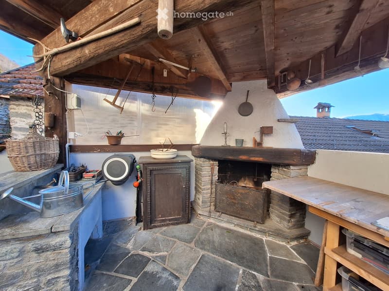 Outdoor kitchen with fireplace, sink, wooden table, storage cabinet, and various kitchen tools hanging on the wall.