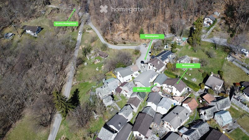 Aerial view of a cluster of houses, one of which is labeled as 'Rustico', another as 'Wohnhaus', with a 'Wendeplatz' and 'Gratis-Parkplatz' indicated.