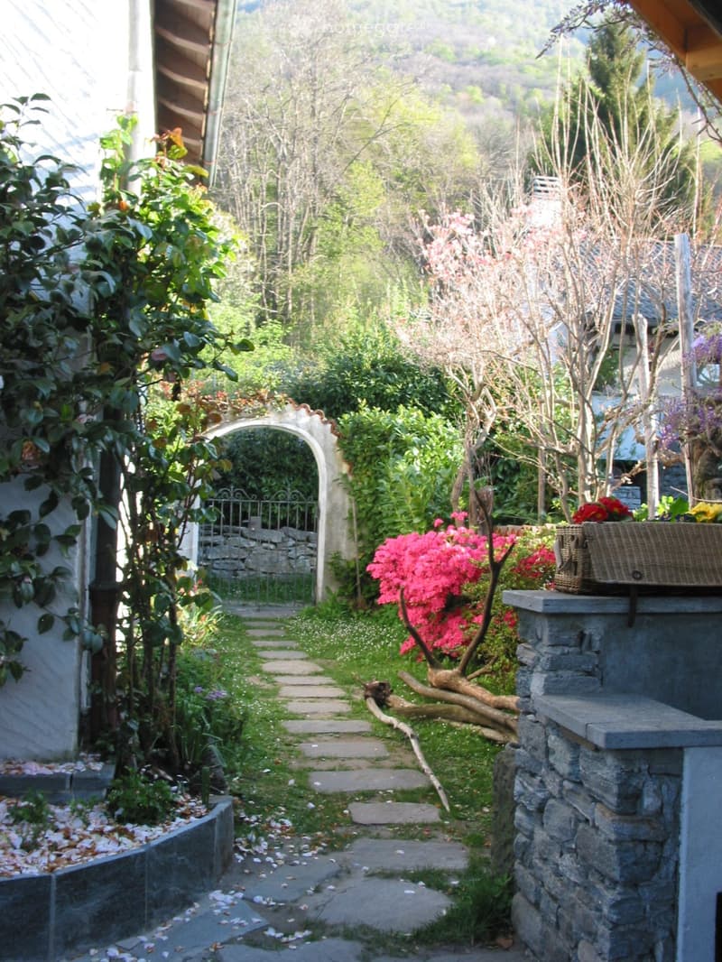 stone pathway, arch entrance, stone wall, flowers, greenery, mountain view