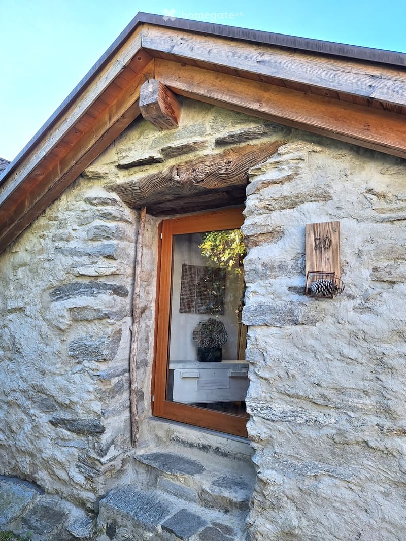 Stone house, wooden door, wooden roof, number 20 on the wall, small window, steps leading to the door