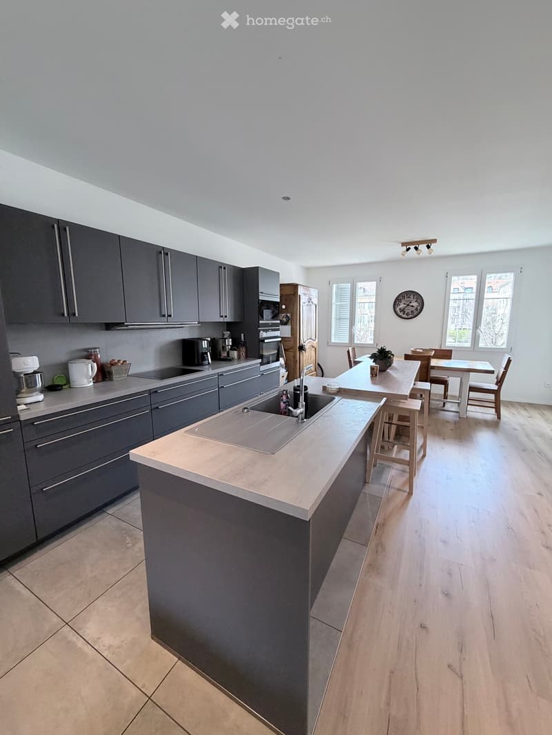 modern kitchen with island, gray cabinets, wooden floor, dining area with table and chairs, wooden cabinet, microwave, coffee maker, kettle, toaster, and other kitchen appliances