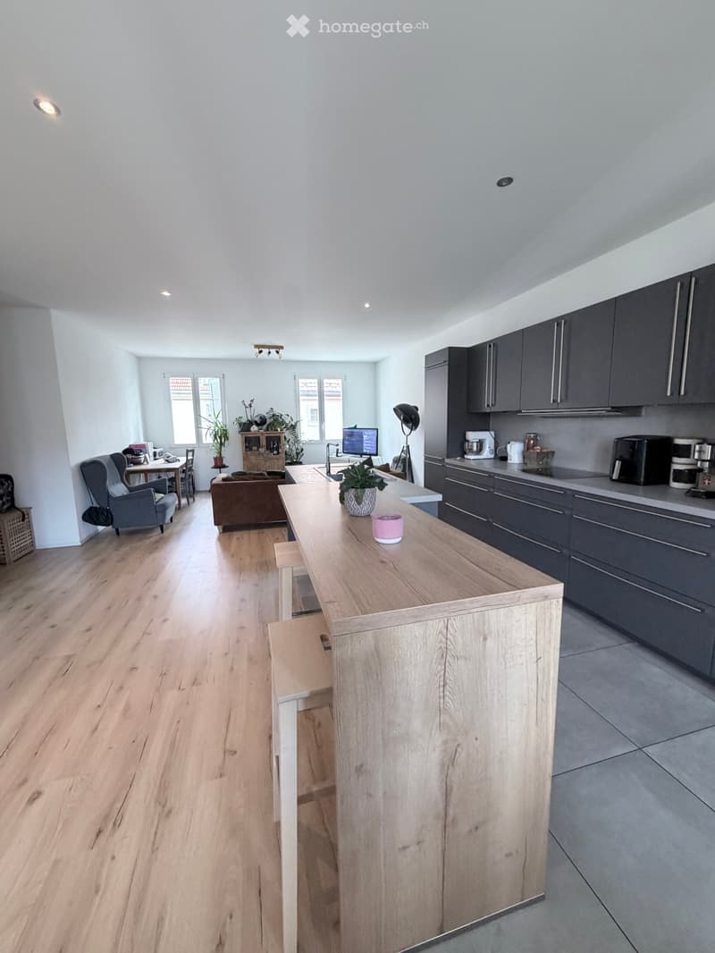 modern kitchen with large island, wooden floor, gray cabinets, white walls, dining table, plants, monitor, coffee machine