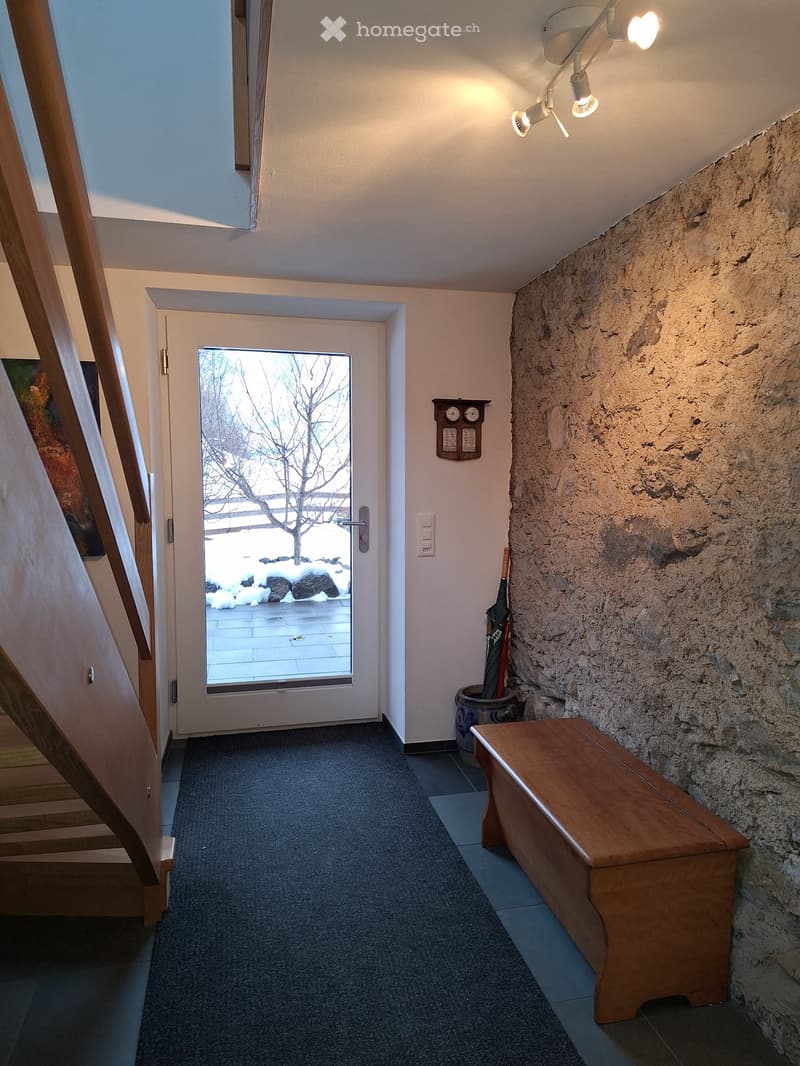 Entrance hall with wooden bench, rug, glass door, wooden stairs, stone wall, mounted lights, umbrella stand