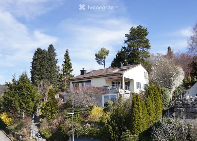 2 story house, white exterior, brown roof, balcony, surrounded by trees and shrubs