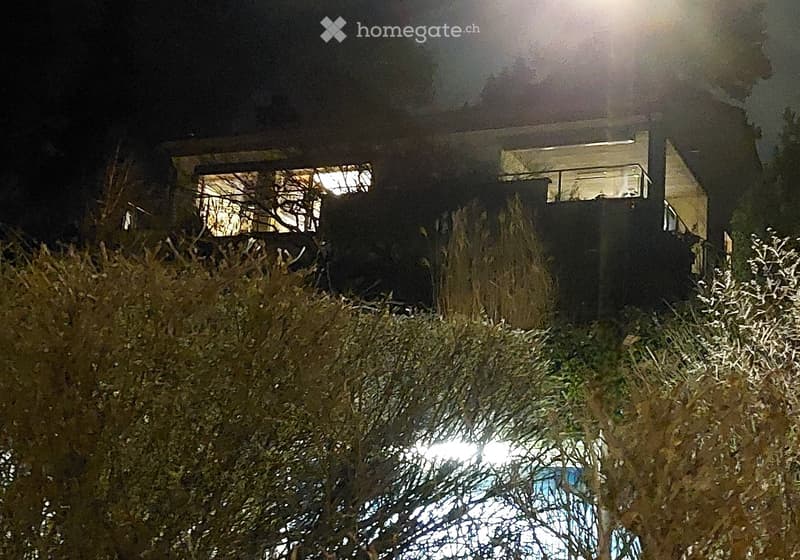 modern house, raised ground floor, large windows, illuminated at night