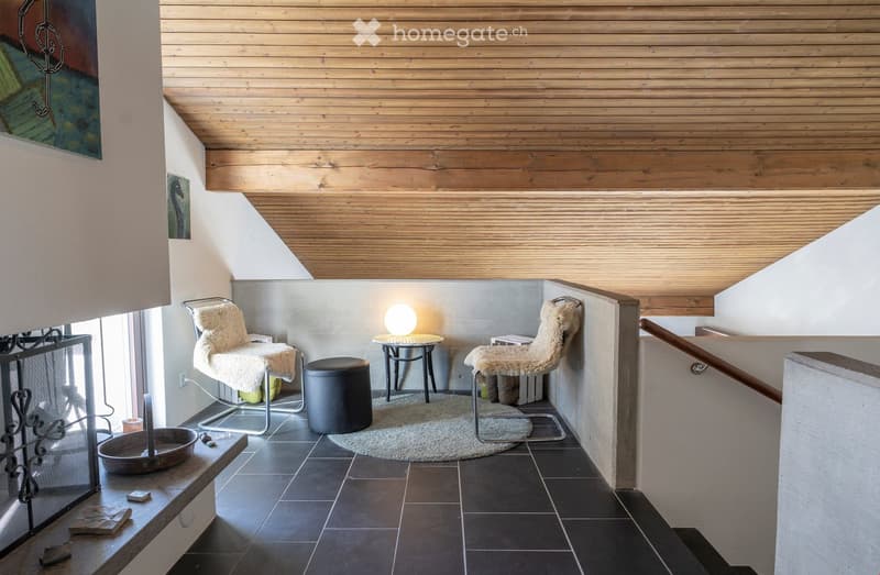 wooden ceiling, black tiles, fireplace, two chairs, round table, lamp, round rug