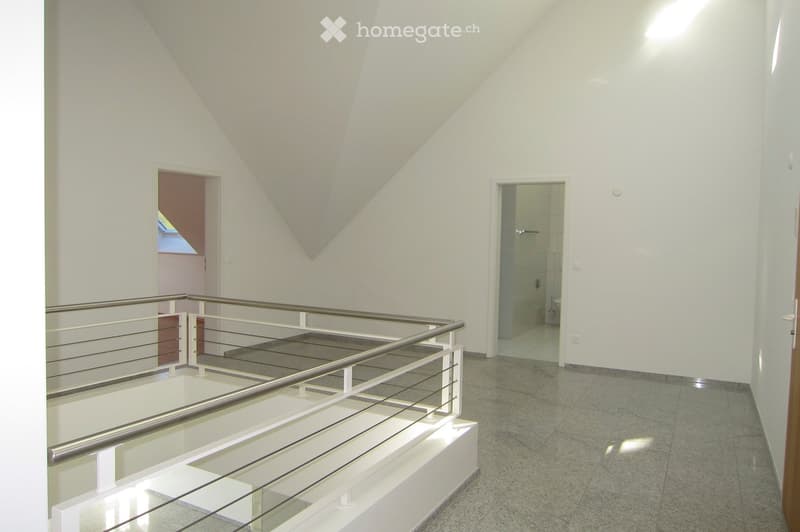 empty room, white walls, gray floor, metal railing, two doors, one leading to a bathroom