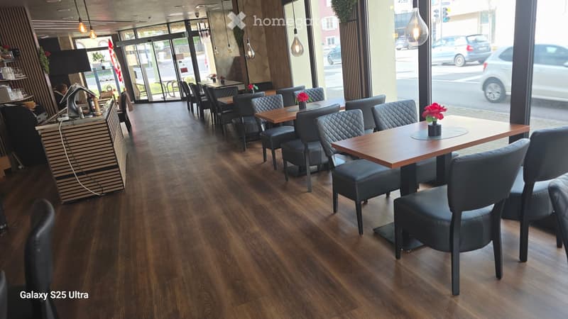 wooden floor, black chairs, wooden tables, flower vases, large windows, view of the street