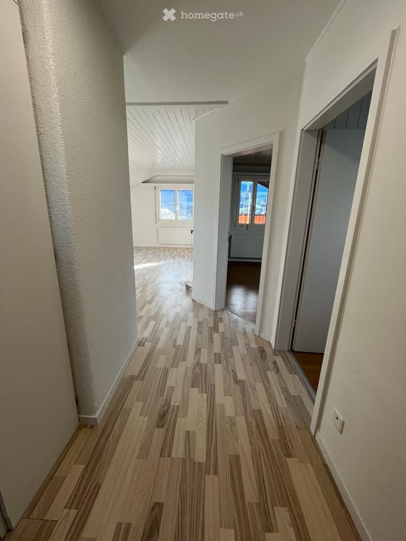 Empty hallway with wooden floor, white walls, two doors, and windows with view