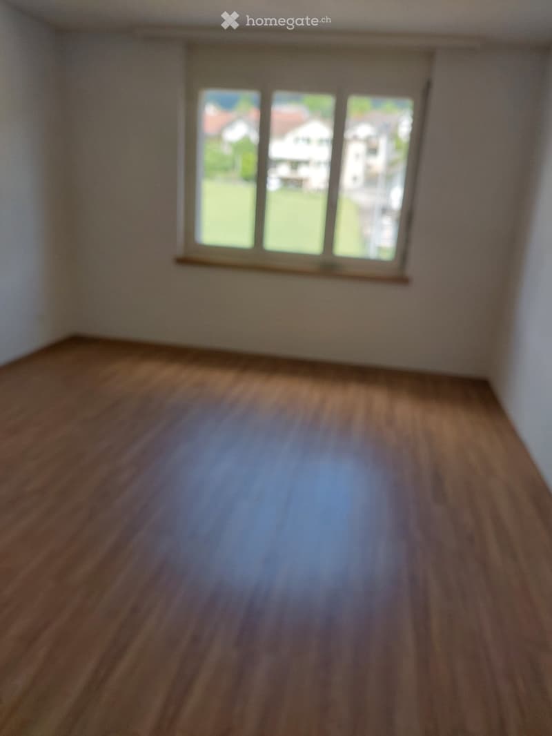 Empty room with wooden flooring and large windows showing a view of the outside. No furniture or equipment is present.