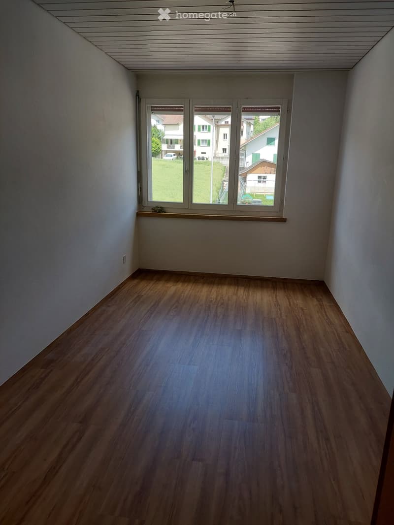 Empty room with wooden flooring and large windows offering a view of the outside area.