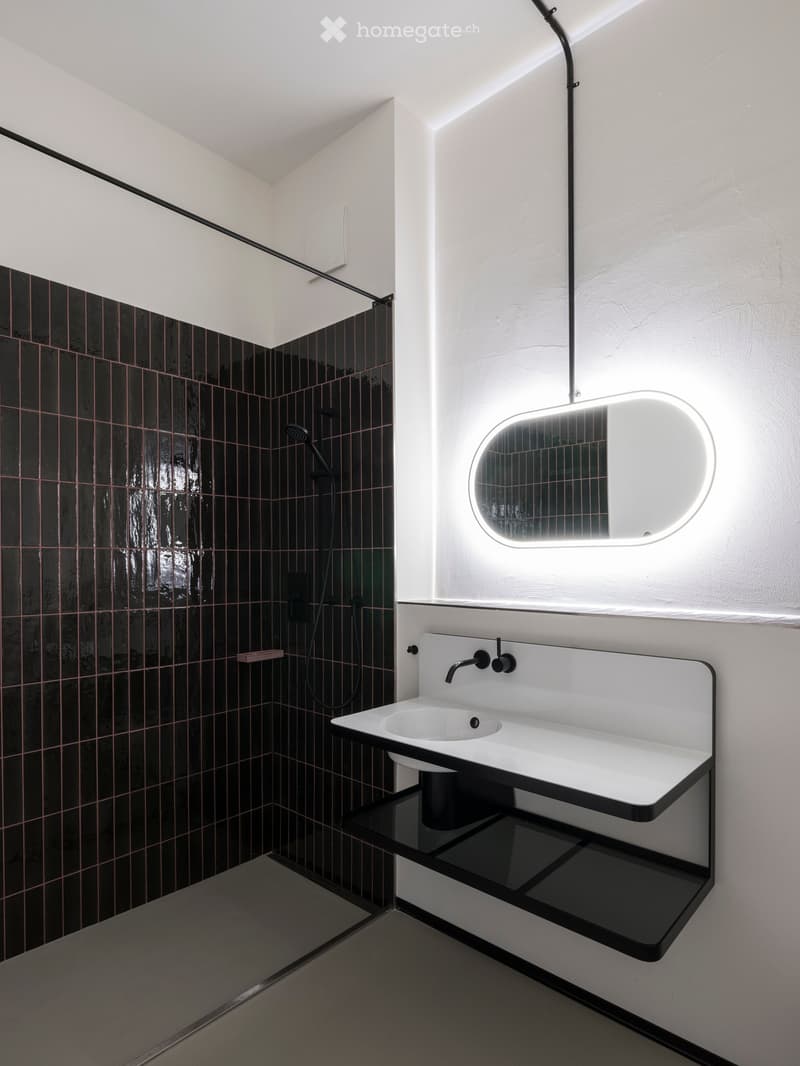 modern bathroom with black tiled walls, white sink, oval mirror, glass shower enclosure