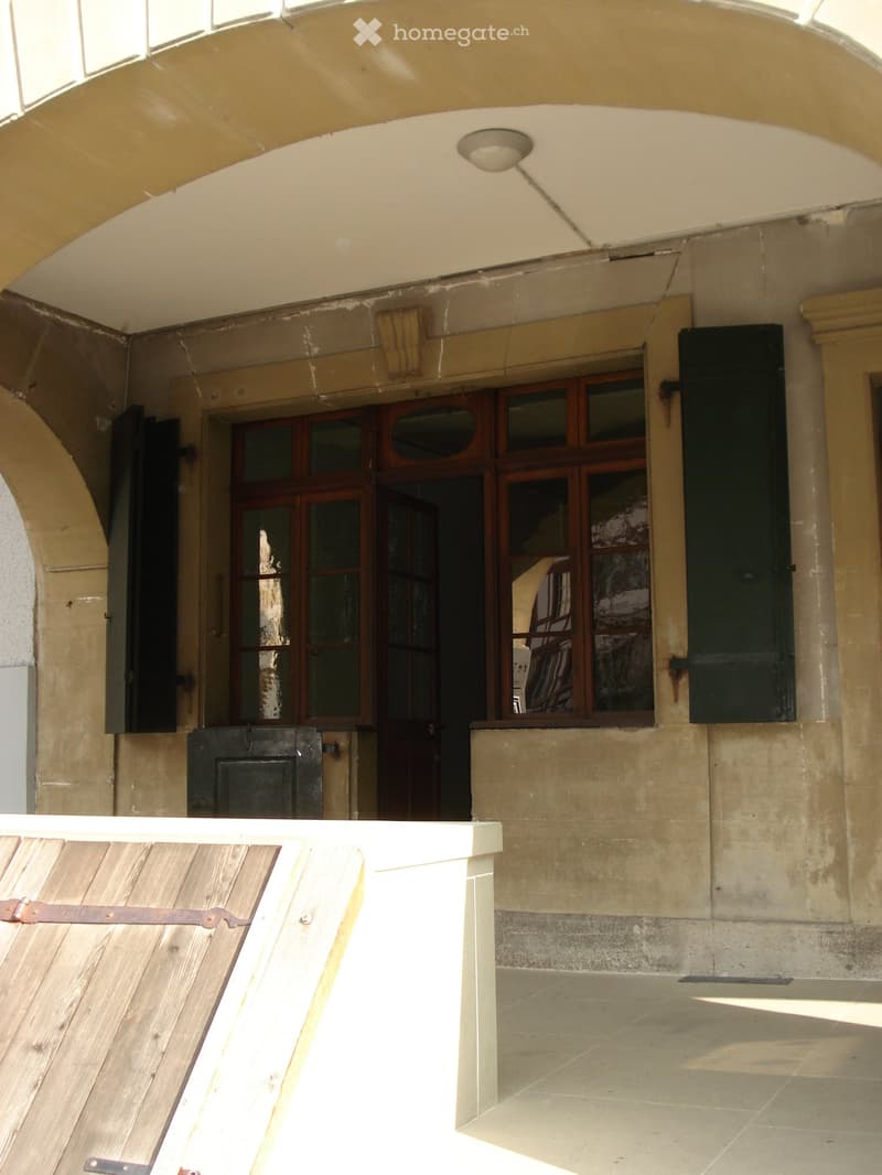 Facade of a building with arched entrance, wooden shutters, and windows with wooden frames
