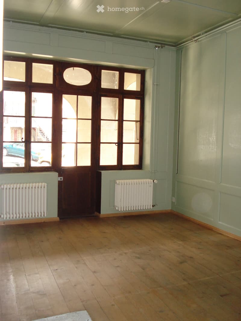 Empty room with wooden floor, white radiators, wooden door, large windows, green walls