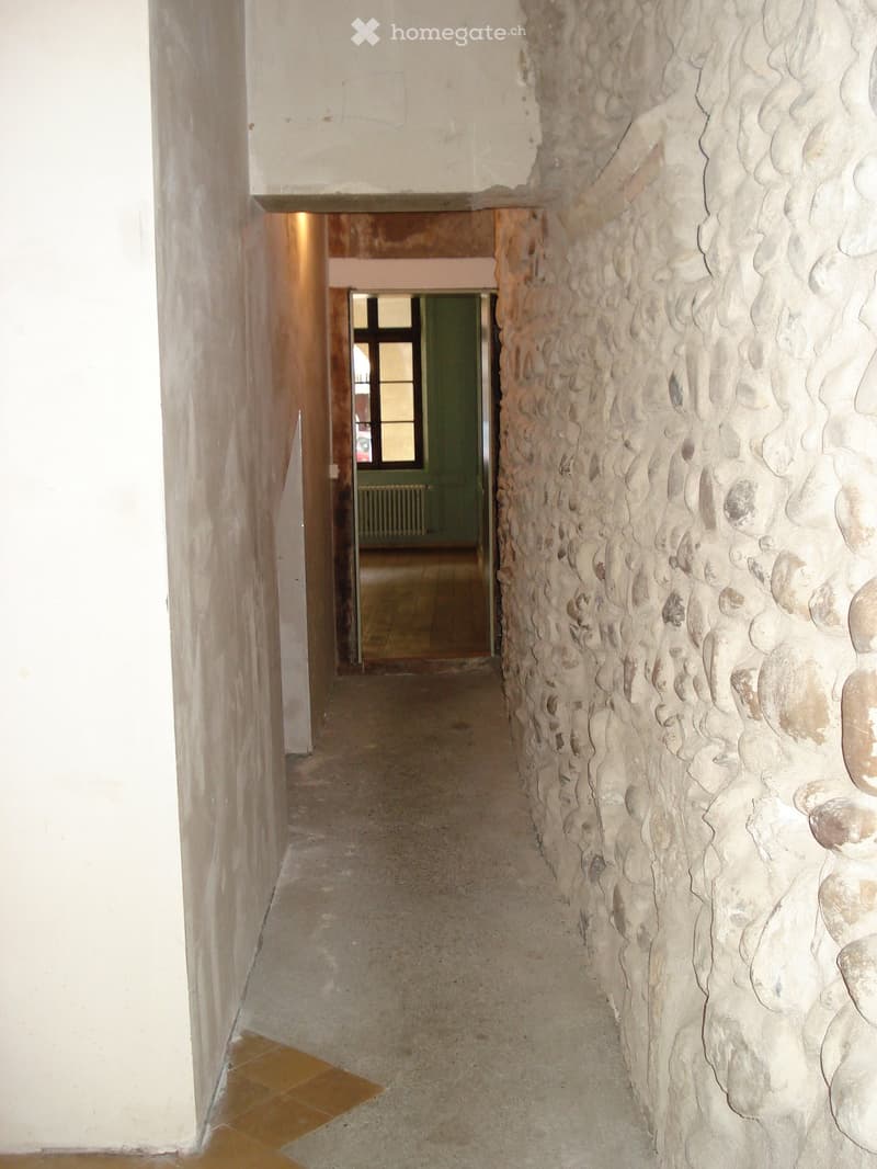 Corridor with stone wall, concrete floor, white walls, open door, window, radiator