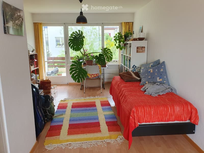 bedroom with bed, rug, chair, large windows with terrace, bookcase, plants, shelves, backpack, guitar