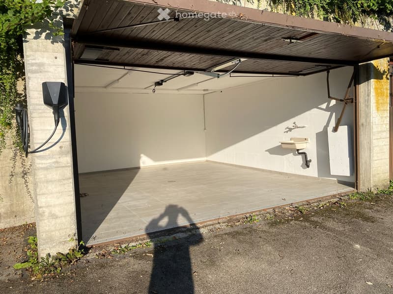 empty garage with tiled floor, wall-mounted sink, electrical outlet, shadow of a person