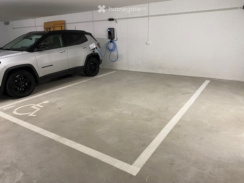 Parking space with charging station, silver SUV parked, white lines marking parking spot, white walls, gray floor