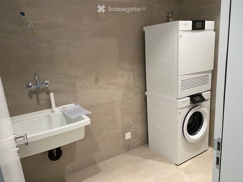 A small laundry room with a white sink, a white washing machine, and a white dishwasher stacked on top of each other.