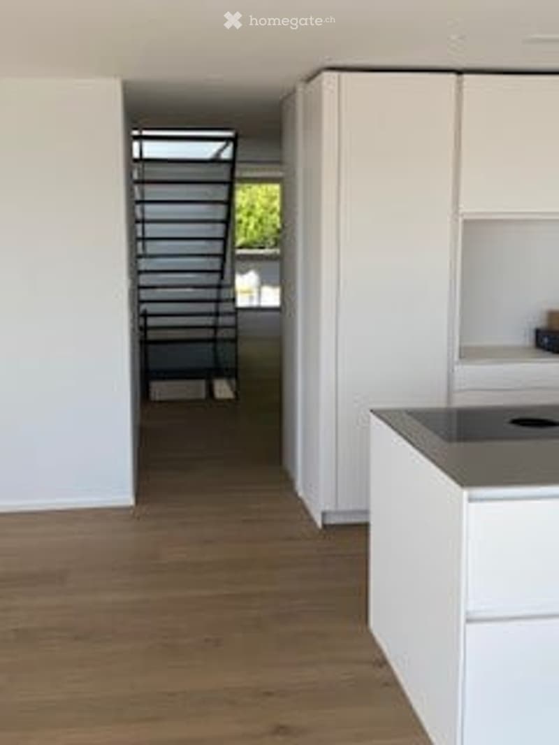 modern kitchen with white cabinets, wooden floor, stainless steel countertop, staircase