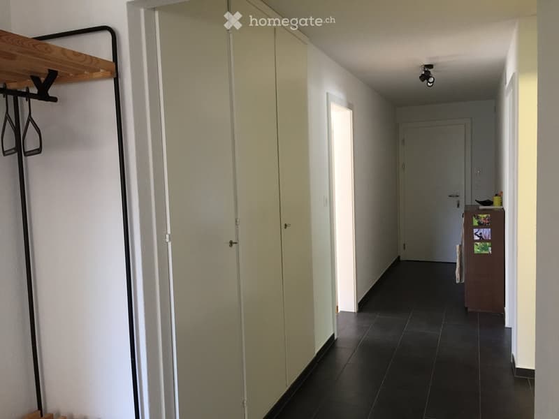 Empty hallway with white walls, black tiled floor, white doors, wooden rack with hangers, small brown cabinet with pictures