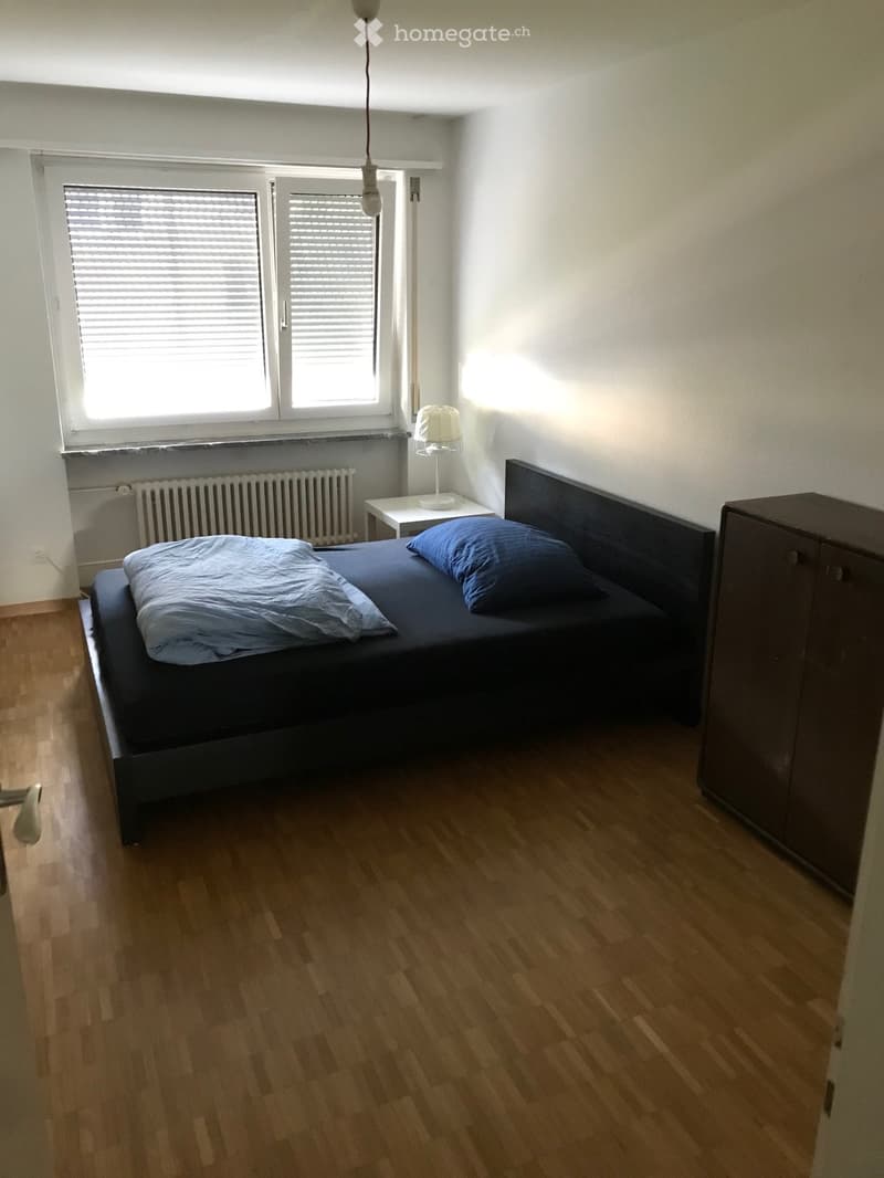Bedroom with bed, nightstand, lamp, radiator, window with blinds, wooden floor, cabinet
