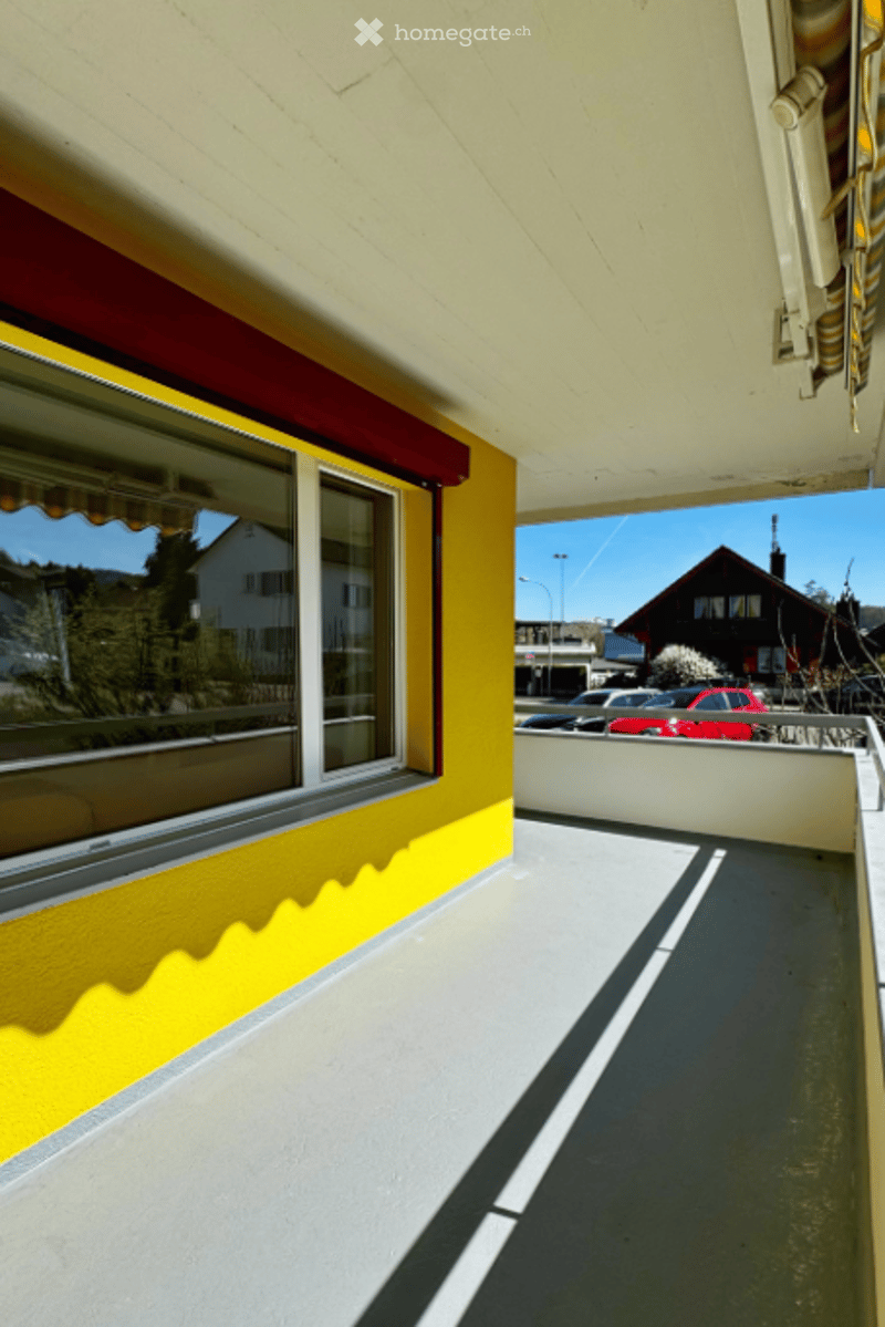 Balcony with yellow wall, white ceiling, glass window, metal railing, shadow on the floor