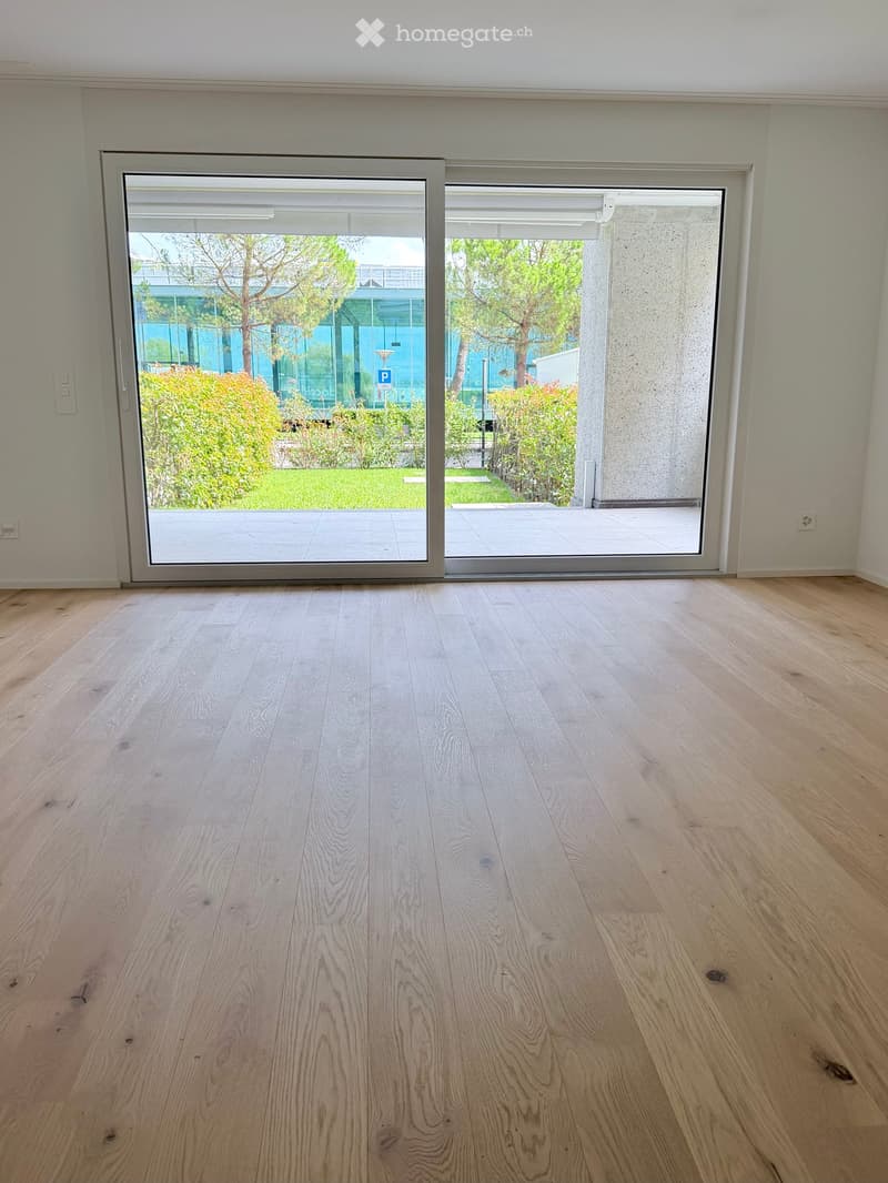 Empty room with light wooden flooring and large sliding glass doors leading to an outdoor area with greenery.