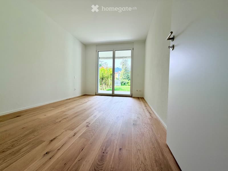 Empty room with light wooden flooring and white walls, featuring a large sliding glass door leading to an outdoor area.
