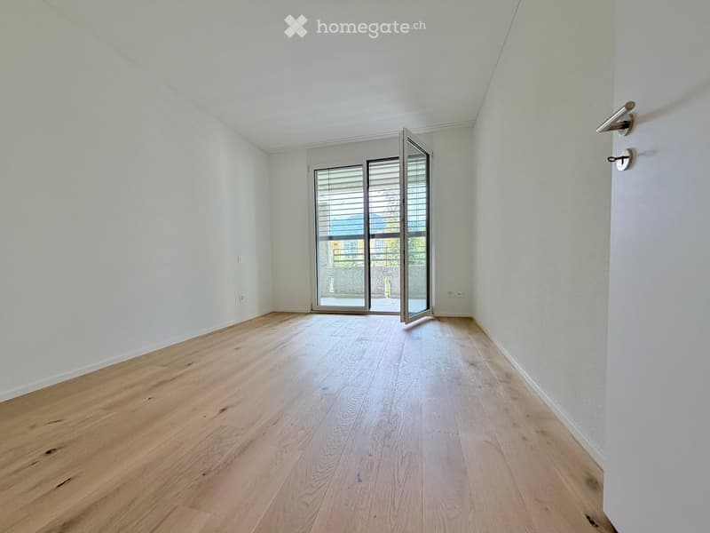 Empty room with light wooden flooring and white walls, featuring a large sliding glass door leading outside.