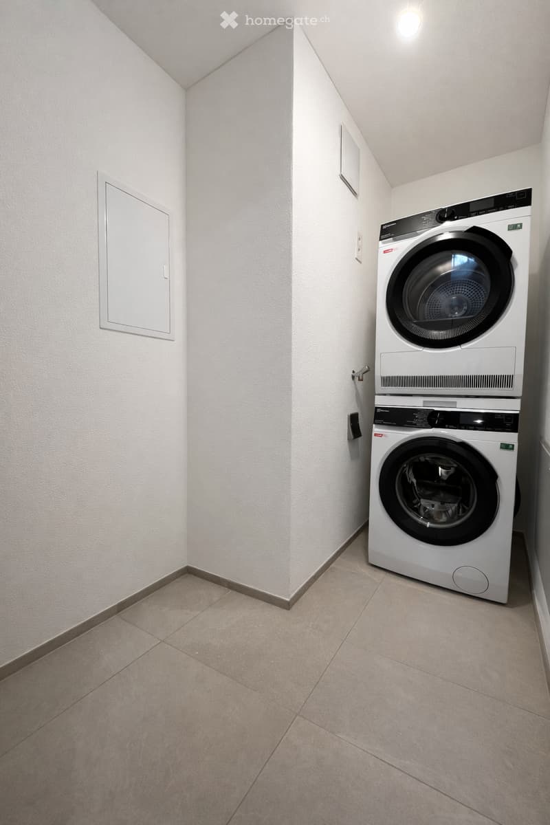 A small room with white walls and tiled floor, containing a stacked washer and dryer.