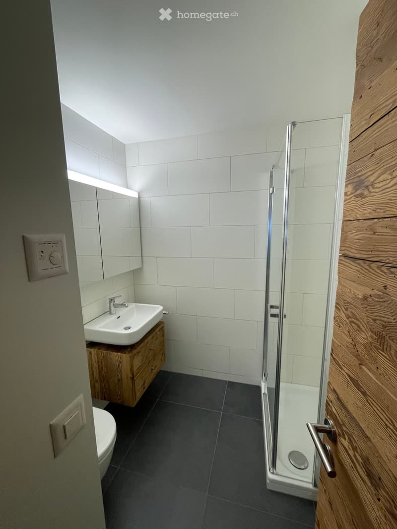 Bathroom with white tiles, wooden cabinet, white sink, glass shower, white toilet