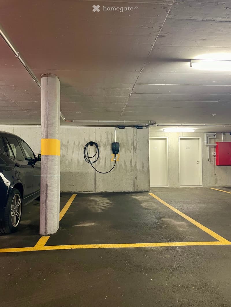 underground parking lot with yellow lines, electric car charging station, two doors, red box on the wall