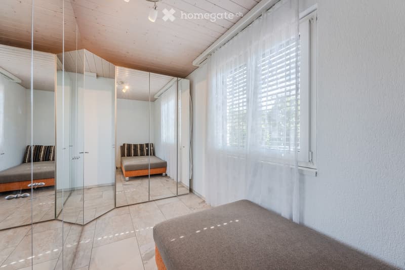 A room with a large mirror, a window with white curtains, a bed, and a small couch